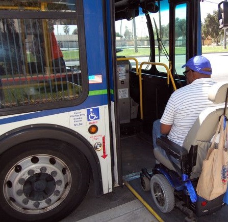 man using a wheelchair boards a bus equipped with a ramp