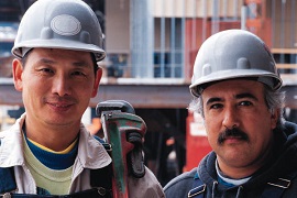 two older men wearing hard hats and carrying tools on a construction site