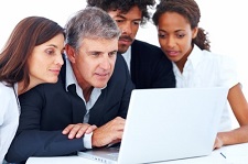 group gathers around older man in front of laptop